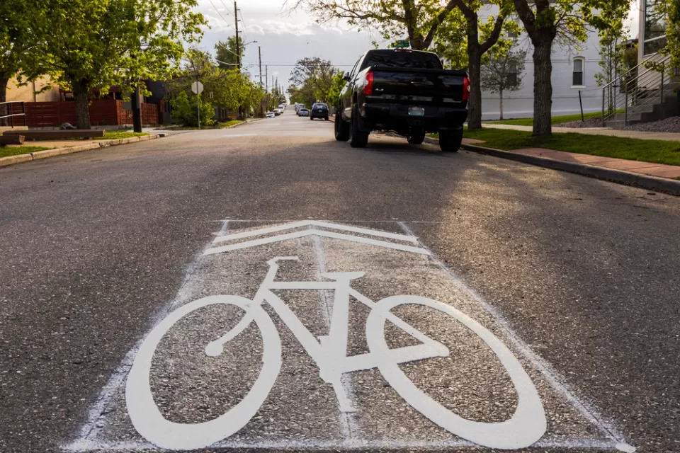 Street-level view of sharrow symbol on asphalt with parked car in background